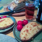 two plates of welsh rarebit served with cherry tomatoes. Beer and bread behind.