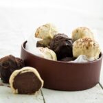 Coffee truffles coated in white and dark chcolate in a box. One broken open in front next to a whole truffle.