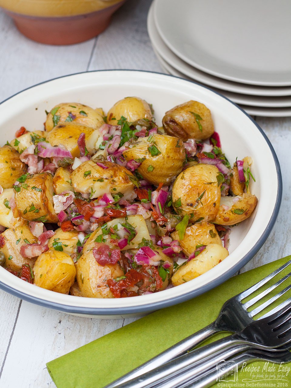 Piquant potato salad in a serving bowl with pile of forks oin napkins in front.
