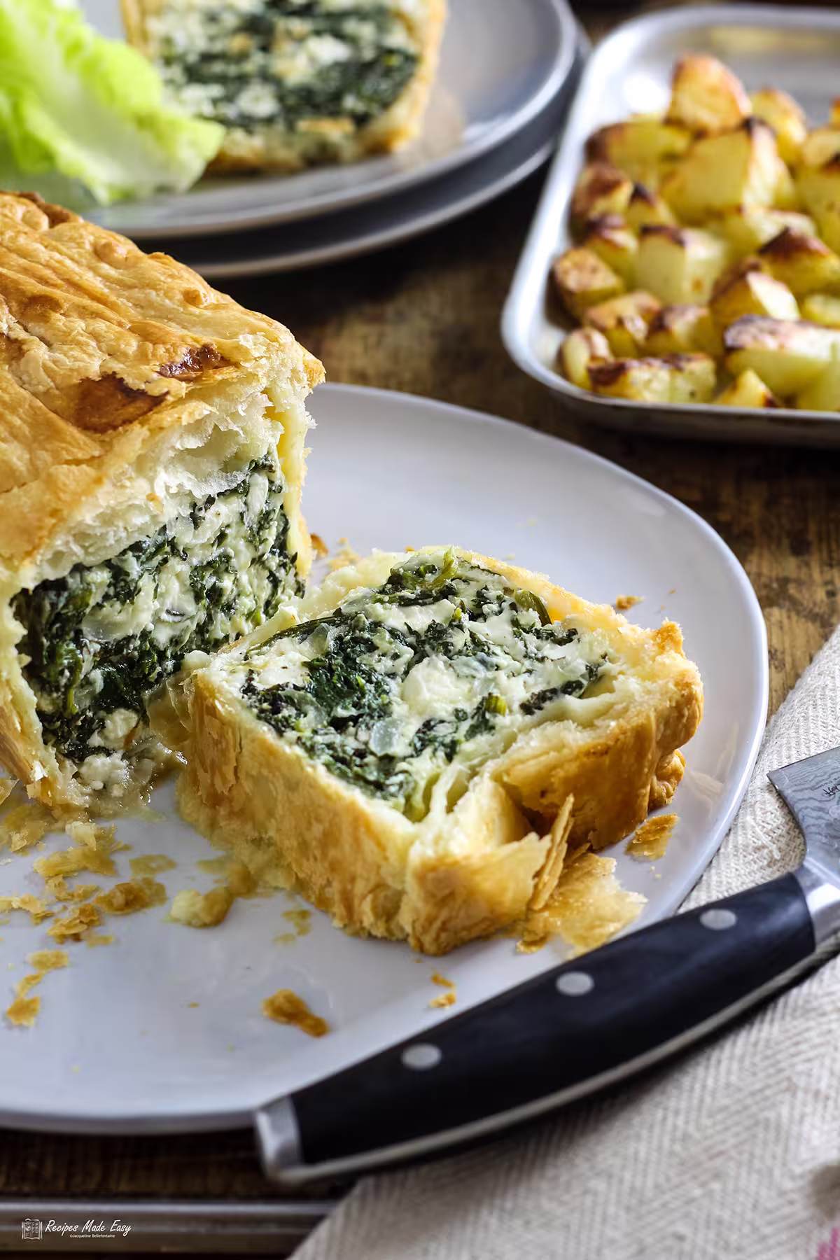 spinach ricotta and feta pie on a white plate with slice laying down to reveal filling.