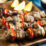 Easy lamb kebabs on a wooden tray served with lemon wedges.