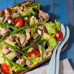 salad nicoise on wooden serving plate with salad tongs on side.