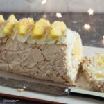 coconut and pineapple meringue roll sliced with knife in front and fairy lights behind.