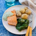 serving of seared salmon with watercress suace on a plate with new potatoes and spinach.
