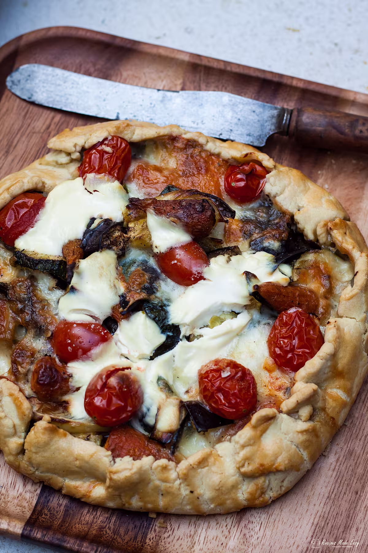 open summer vegetable pie on wooden board with old knife.