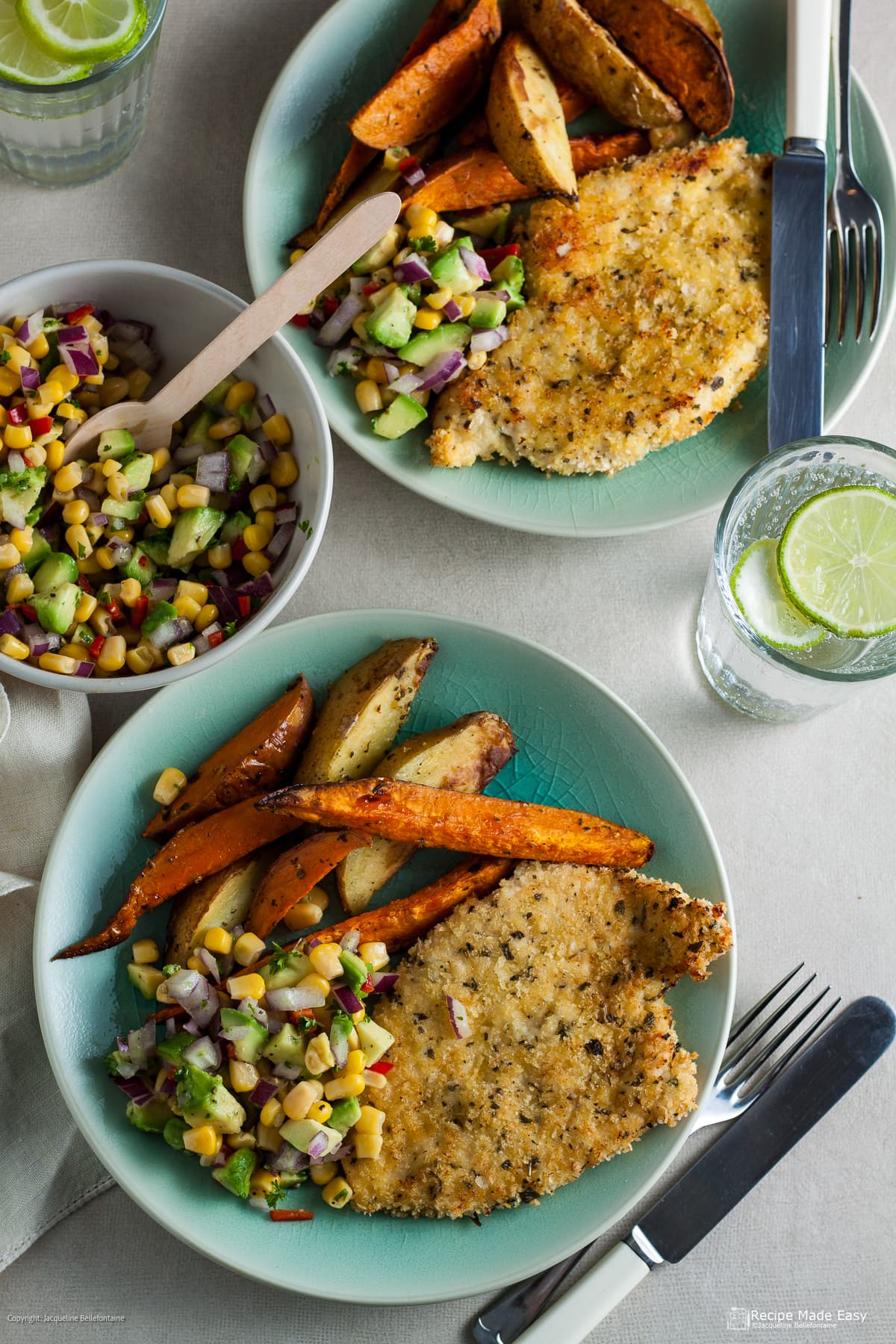 2 plates of oven baked chicken schnitzel served with sweet potato and potato chips with a bowl of salsa on the side and water glasses.