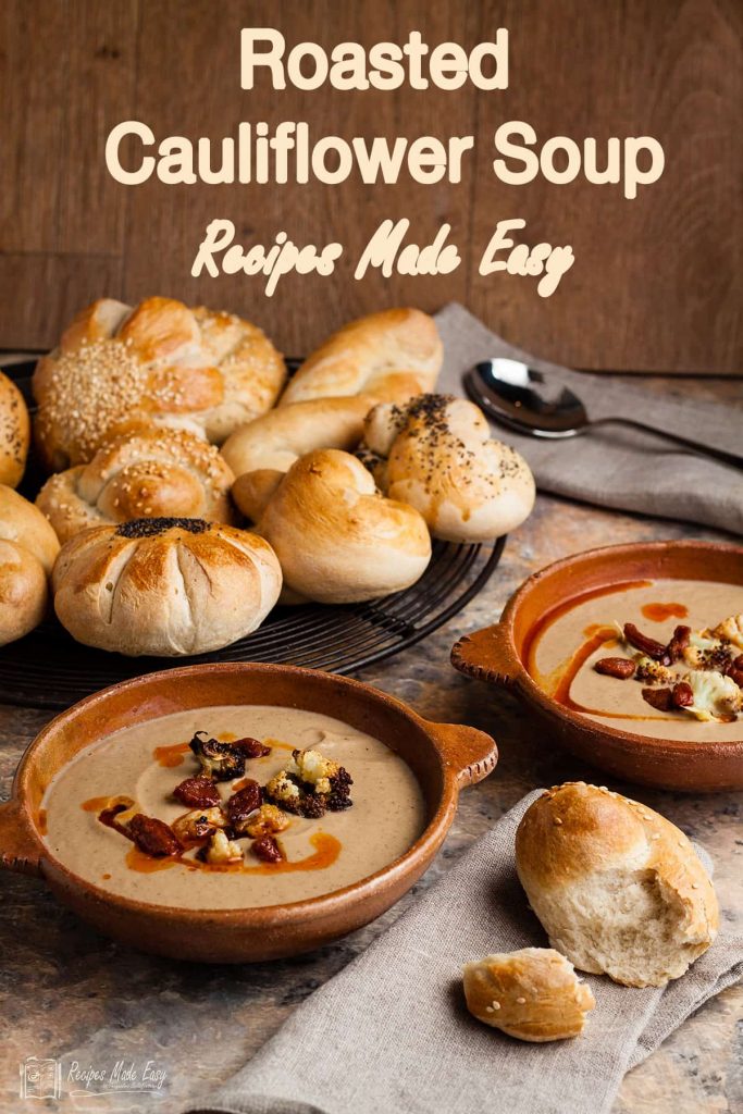 bowl of roasted cauliflower soup with plate of bread rolls behind.