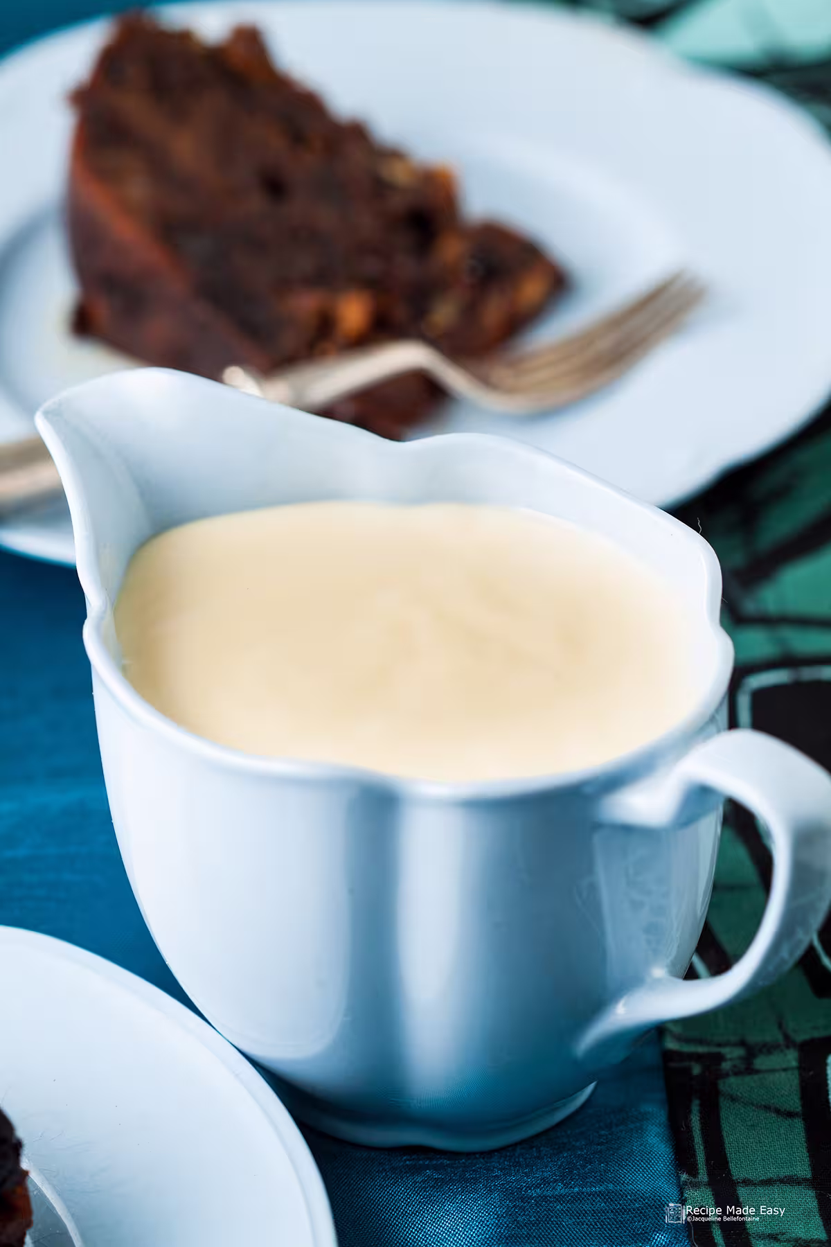 brandy sauce ib=n a blue jug with a serving of Christmas pudding behind.